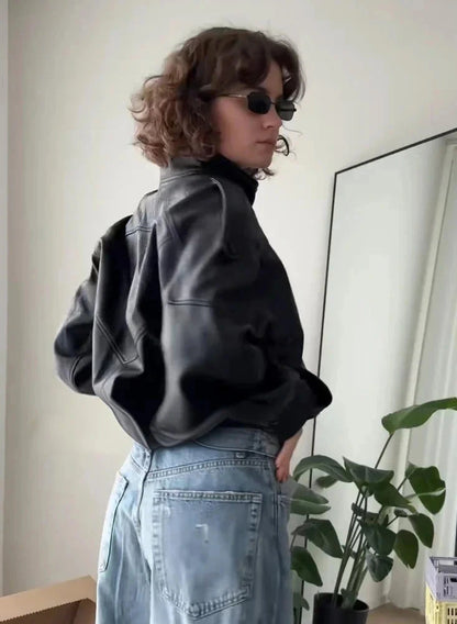 Black loose PU leather jacket with a zip front and side pockets displayed on a hanger against a neutral background.