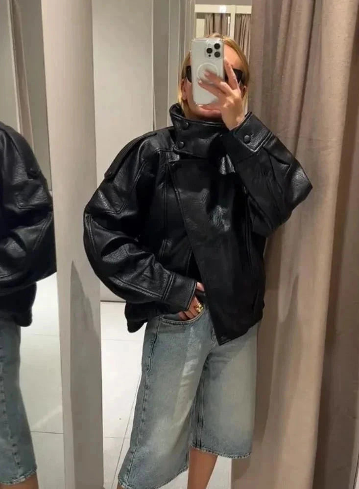 Black loose PU leather jacket with a front zipper and side pockets, displayed on a hanger against a neutral background.