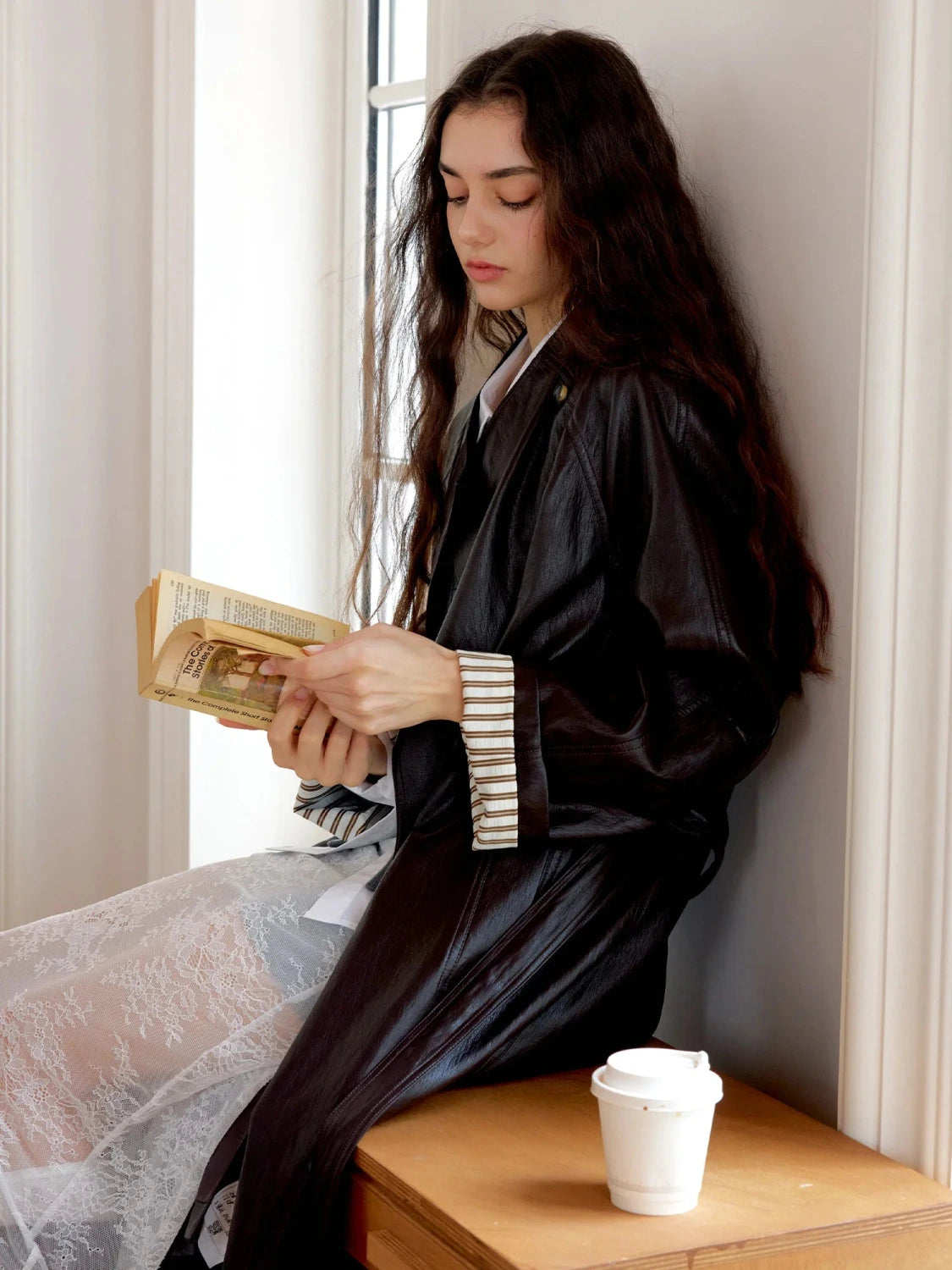 Elegant long overcoat in faux leather with a stand-up collar and belted closure, suitable for casual and formal wear.