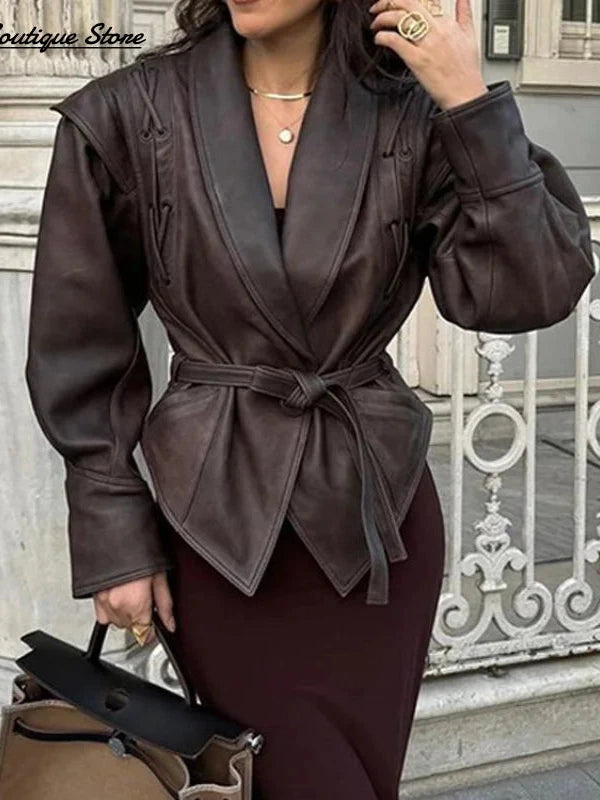 Vintage brown leather jacket with padded shoulders, belt closure, pockets, and turn-down collar. Regular length and tailored